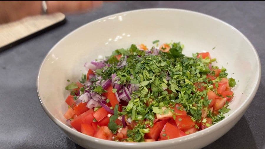 Pico de gallo ingredients in a white bowl: diced tomatoes, red onions, fresh cilantro, and green chili before mixing.