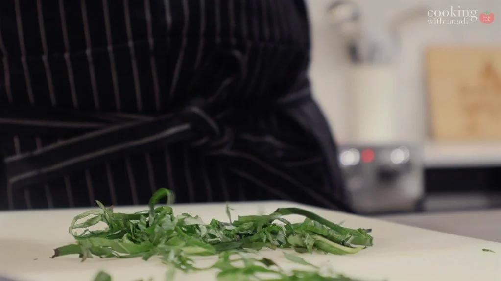 Chopped green onions and cilantro on a white cutting board during deviled egg preparation.
