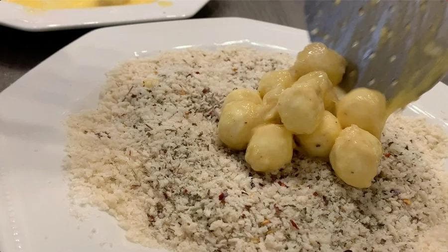 Mozzarella balls coated in breadcrumbs on a white plate with green olives on a fork.