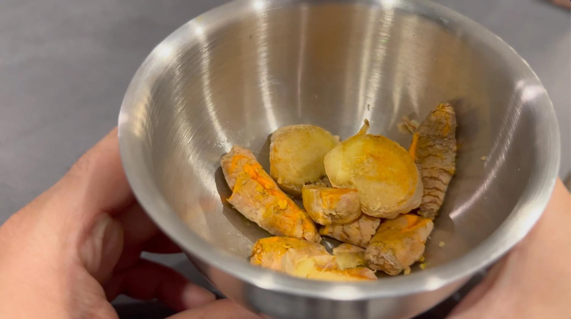 Smashed turmeric root and ginger pieces in a stainless steel bowl, ready to be added to saucepan.