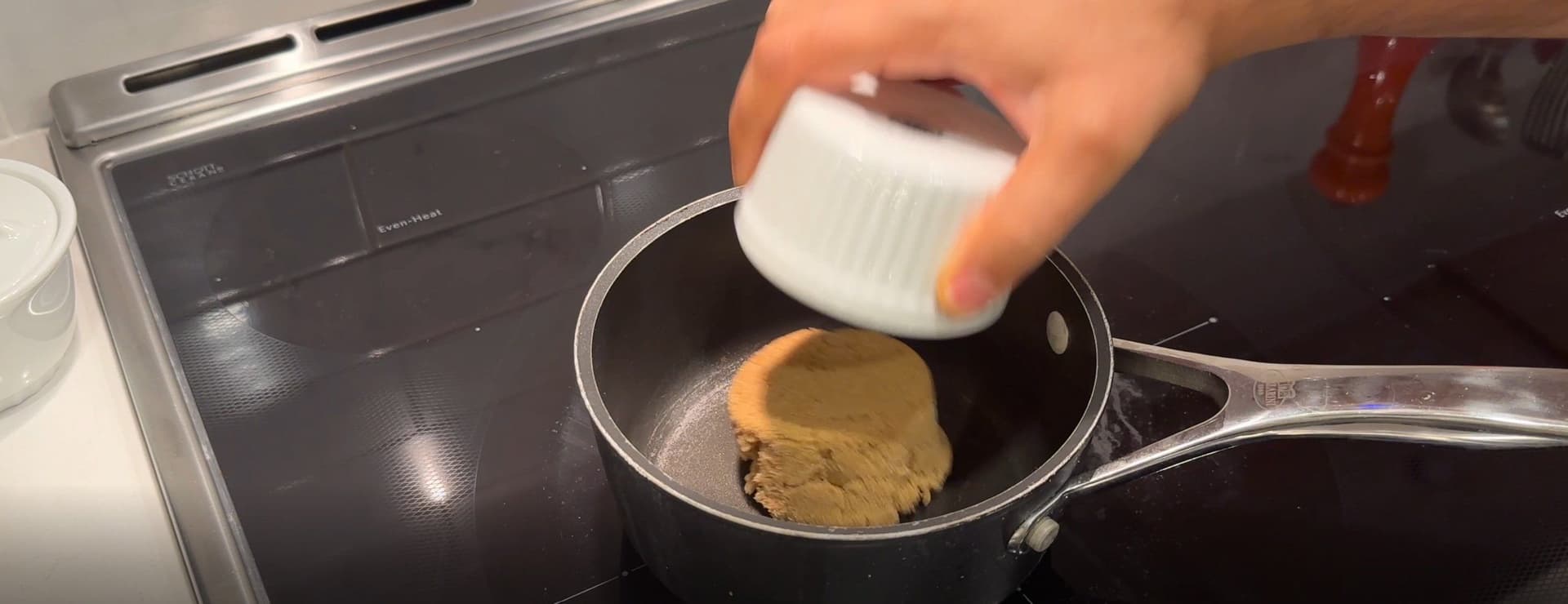 Pouring vanilla extract into a saucepan with dissolved brown sugar mixture on the stovetop.