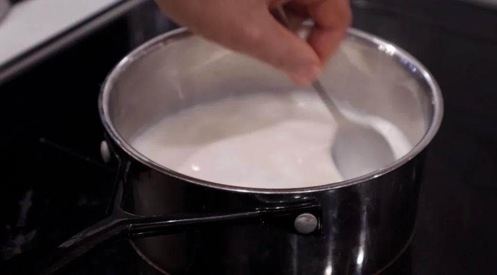 Warm milk being stirred in a black saucepan on the stovetop.