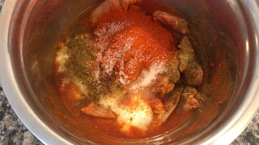 Chicken pieces coated in red yogurt marinade with garam masala and spices in a bowl.