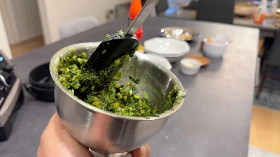 Homemade spinach pesto in a mortar with pestle, showing coarse green paste texture.