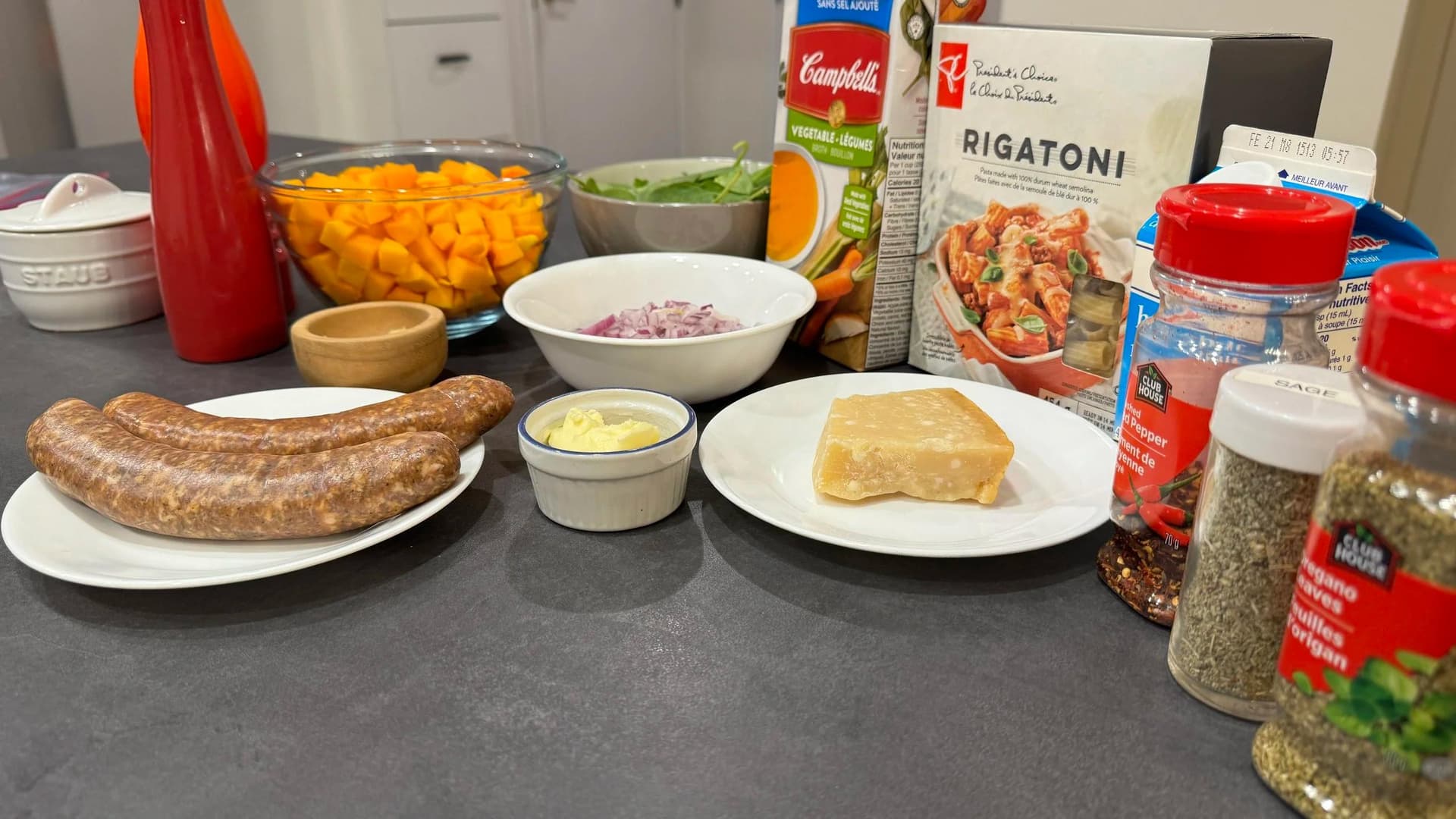 Ingredients for butternut squash sausage pasta: sausage, butter, diced onions, rigatoni pasta, and spices arranged on counter.