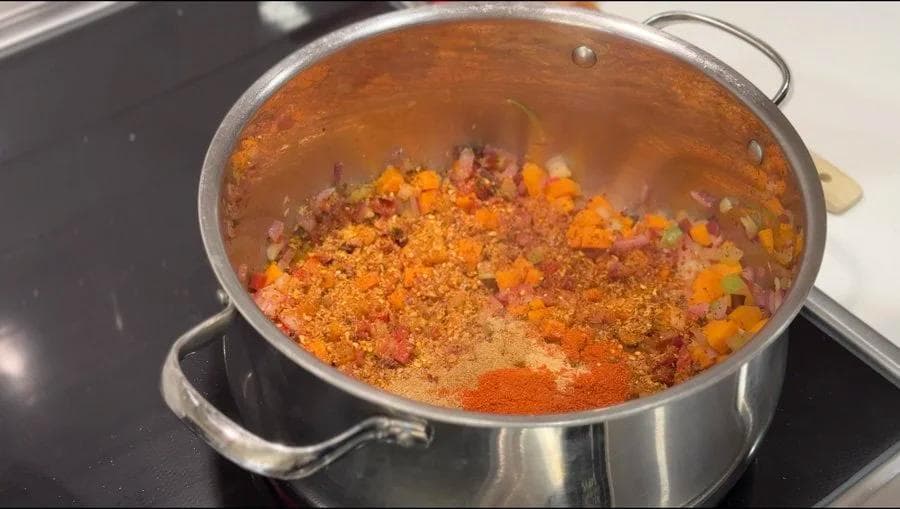 Sautéed diced onions, carrots, and peppers with spices including paprika and cayenne in a large pot.