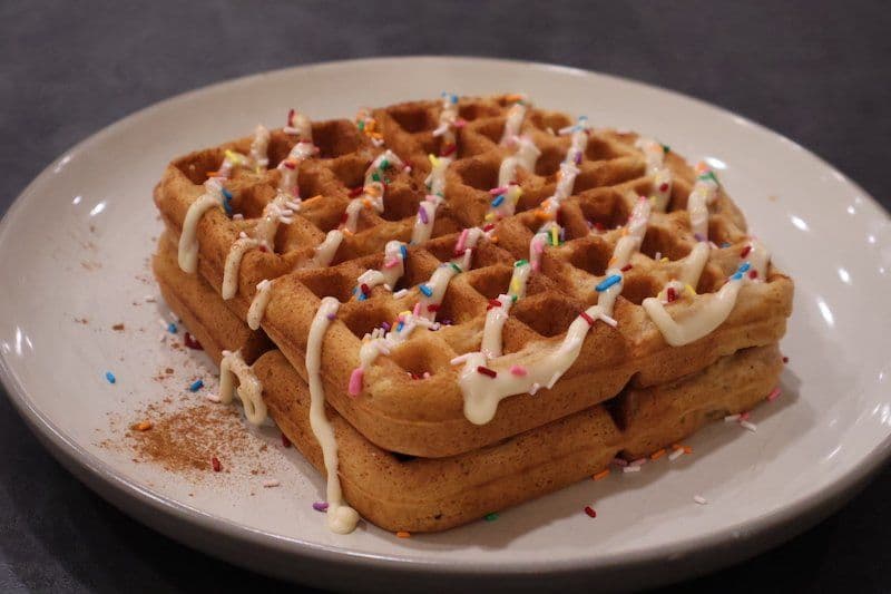 Sugar cookie waffle drizzled with white icing and colorful sprinkles on a white plate.