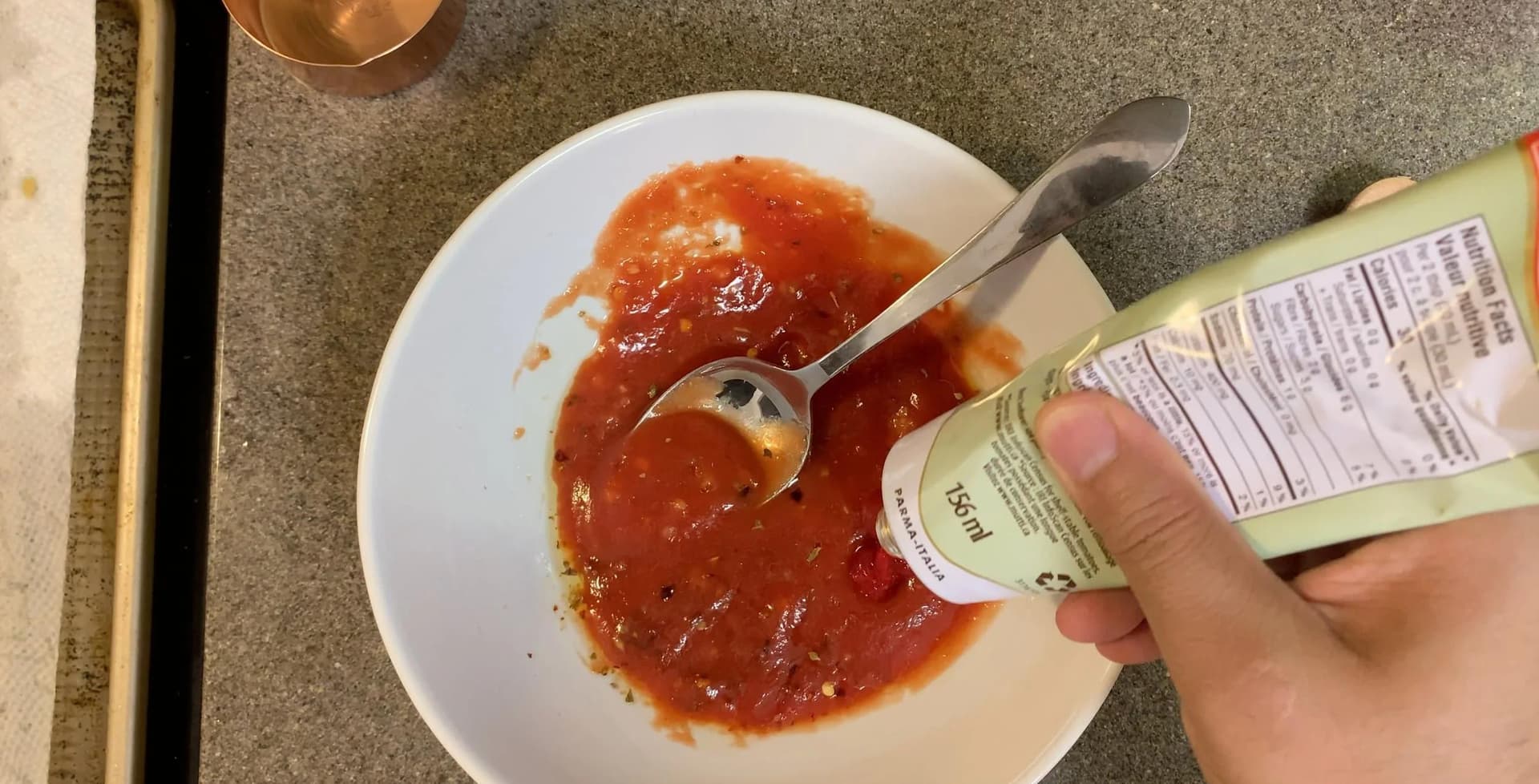 Tomato paste being stirred into red pizza sauce in a white bowl with a spoon