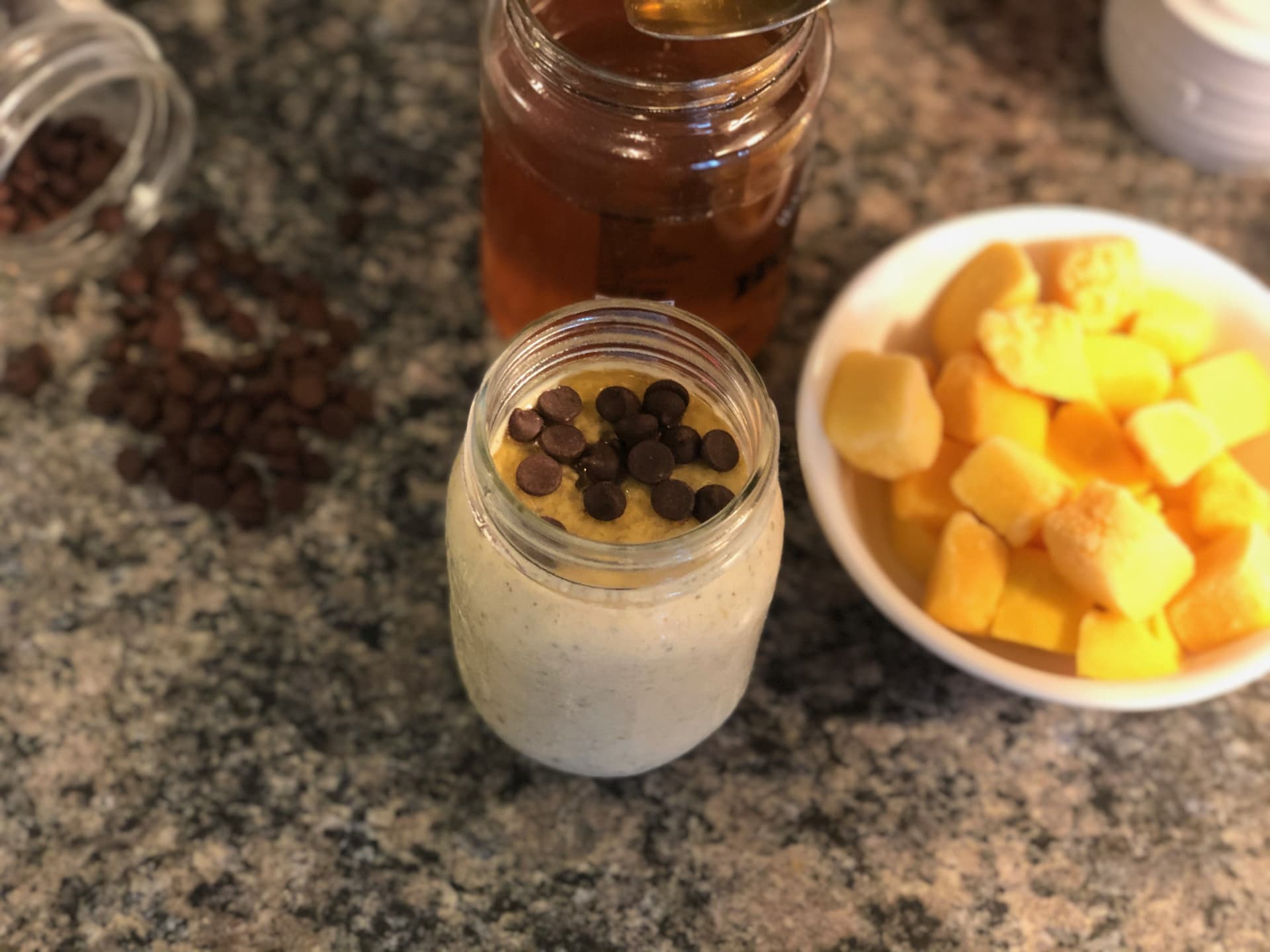 Chocolate chip mango overnight oats in a jar with fresh mango chunks and chocolate chips on the side.