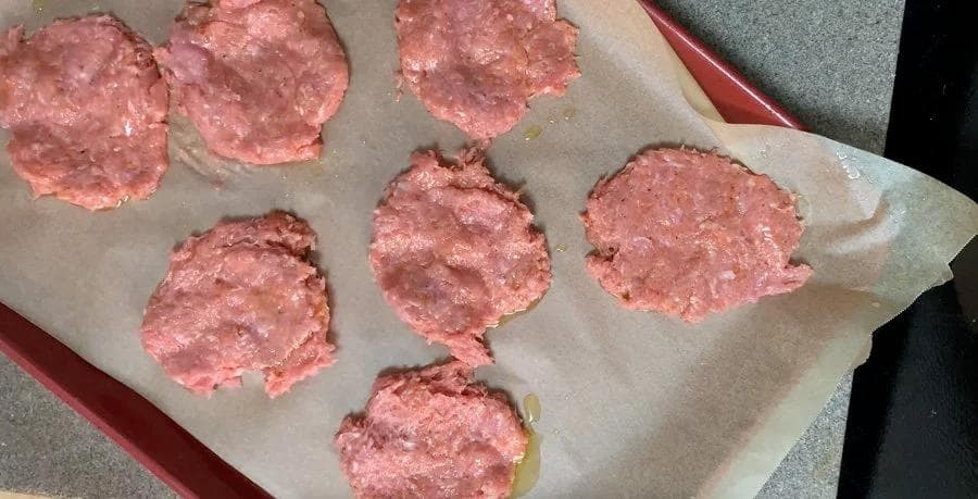 Seven raw breakfast meat patties on parchment paper, ready to refrigerate before cooking.