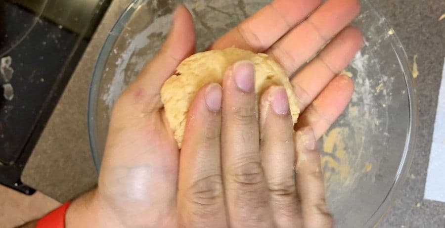 Hand holding an oblong-shaped dough portion, showing the formed hashbrown mixture before frying.