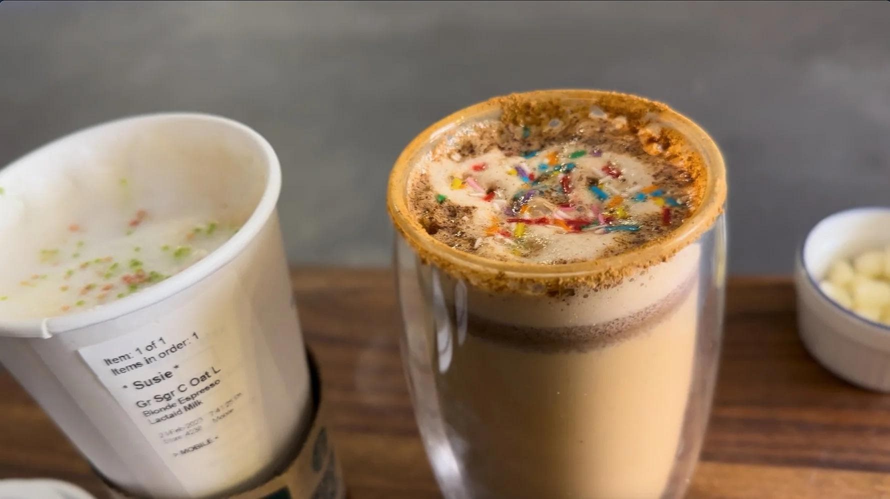 Homemade sugar cookie lattes in glasses topped with cinnamon sugar rim and colorful sprinkles, displayed on wood surface.