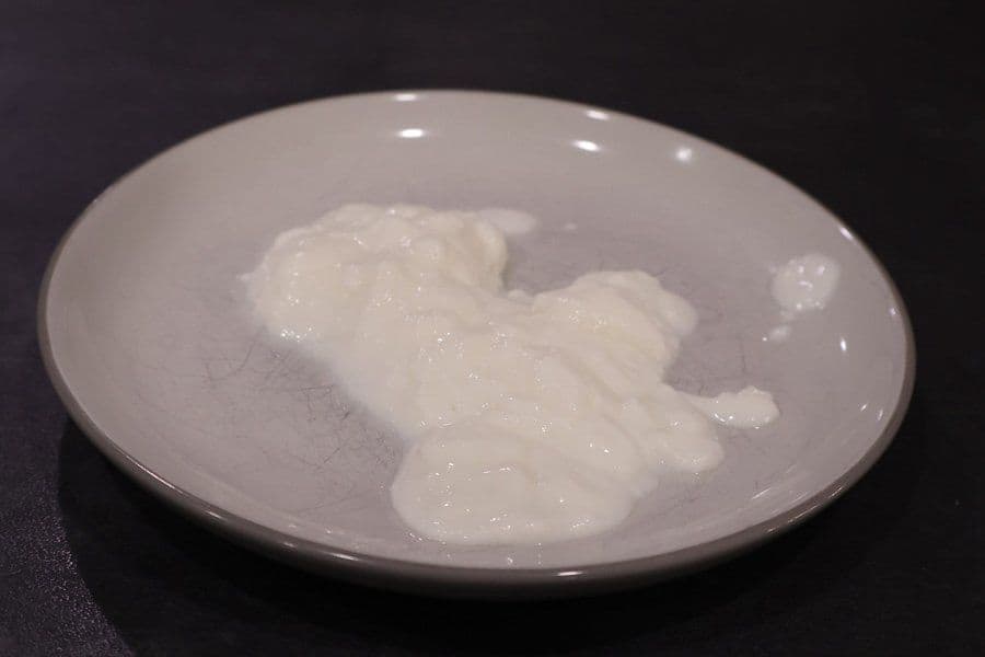 Thick, creamy white hung curd dolloped in a shallow gray ceramic bowl on a dark surface.