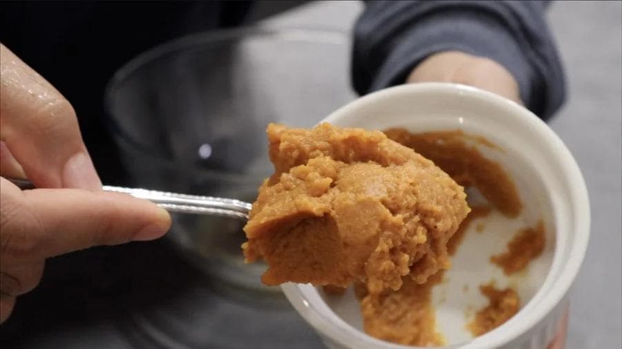 Hand holding spoon with pumpkin cookie dough over white bowl of dough mixture.