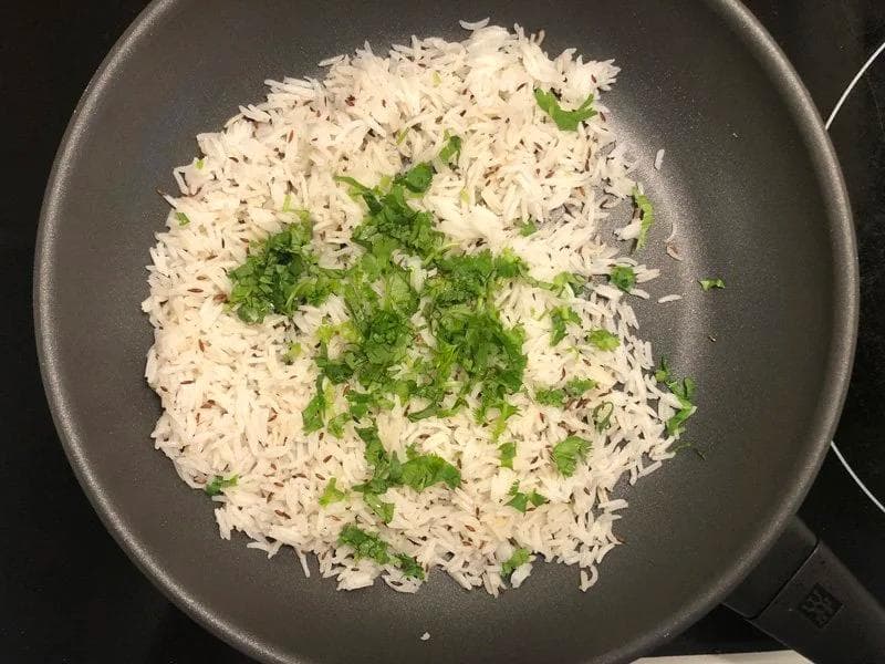Cooked white rice mixed with fresh cilantro in a dark pan, showing the finished rice ready to be seasoned.
