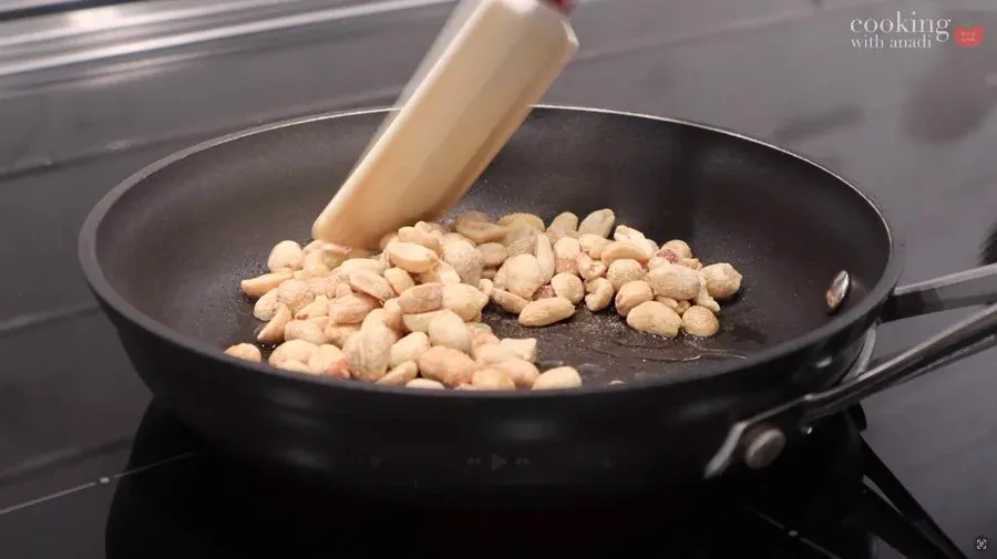 Roasting peanuts in a black pan with a wooden spoon, cooking over medium heat until golden brown.