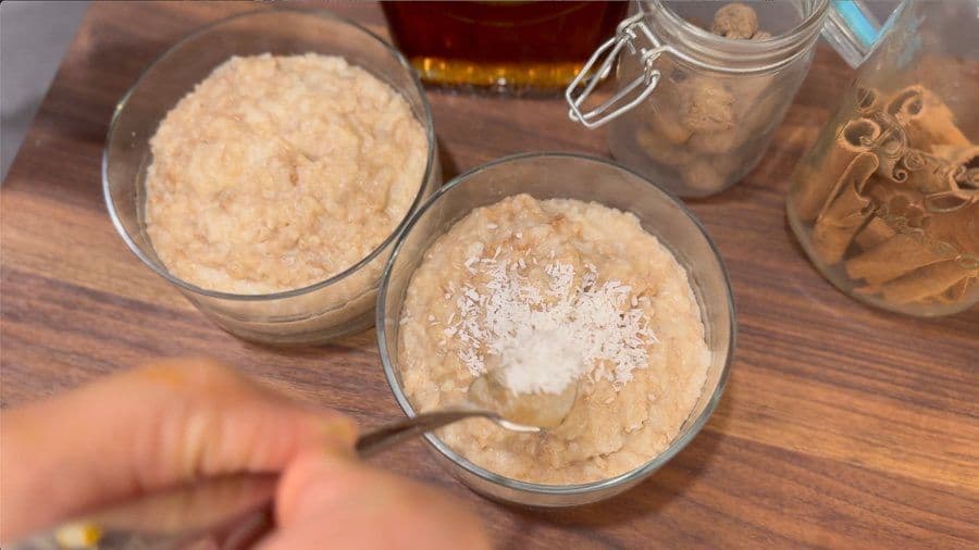 Two bowls of creamy arroz con leche topped with coconut flakes and ground cinnamon on a wooden surface.