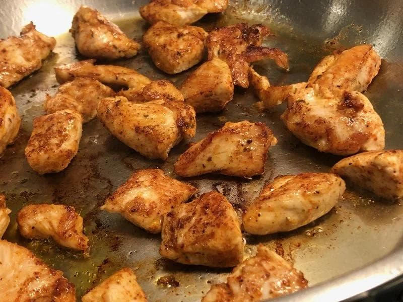 Cajun-seasoned chicken pieces searing in a pan with golden-brown, spiced coating.