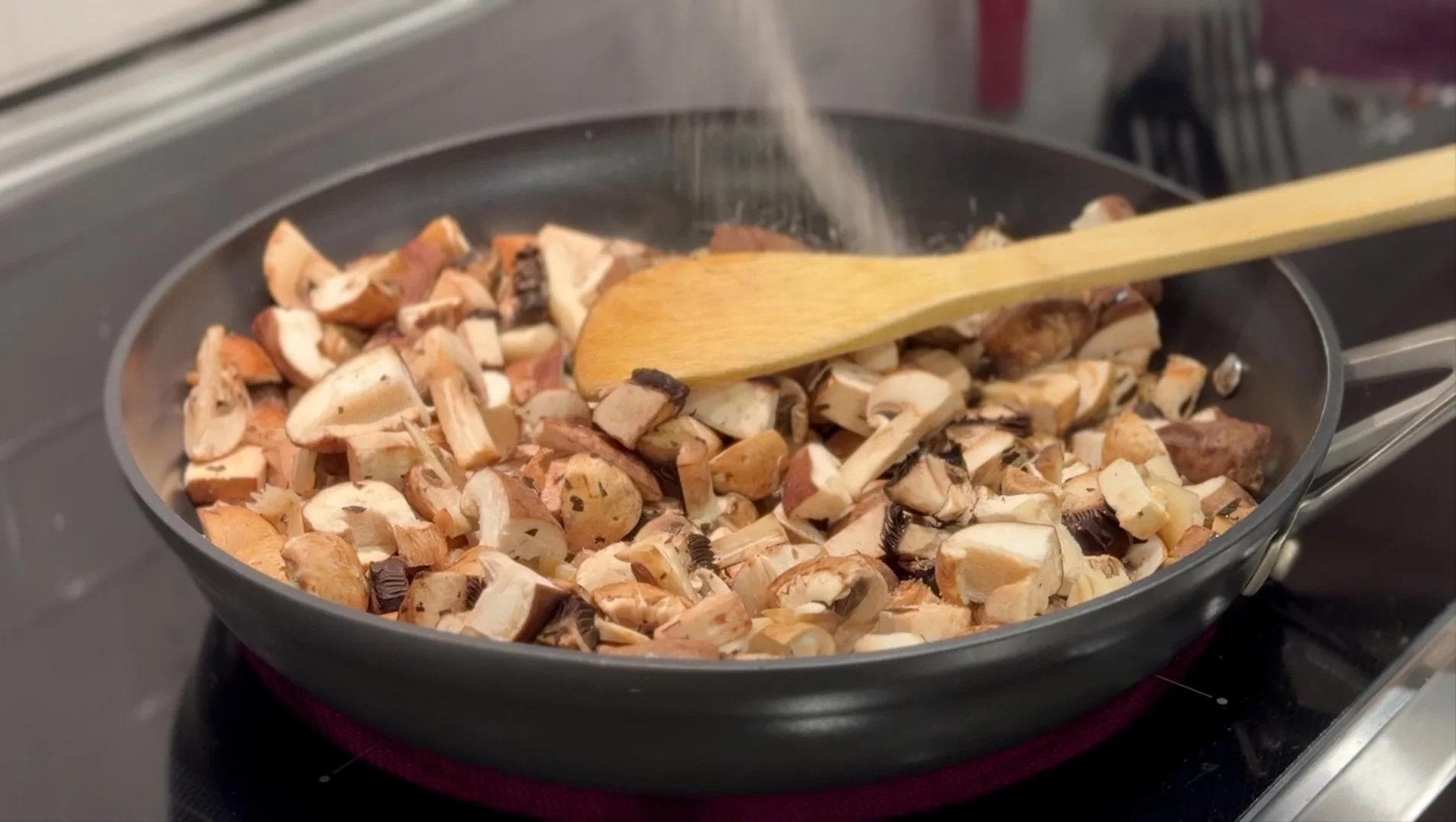 Diced mushrooms cooking in a dark skillet with a wooden spoon, releasing moisture during the initial cooking stage.