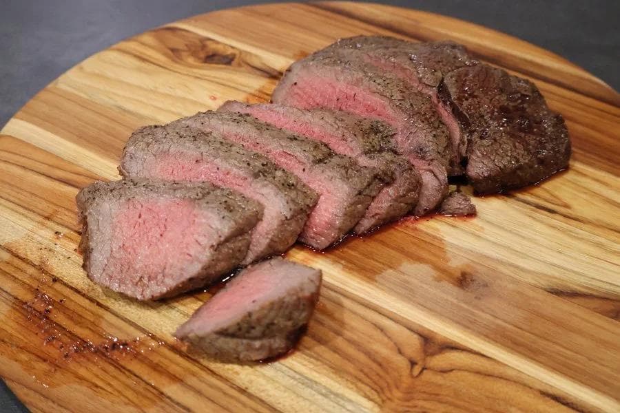 Sliced medium-rare steak on a wooden cutting board showing pink center and seasoned crust.