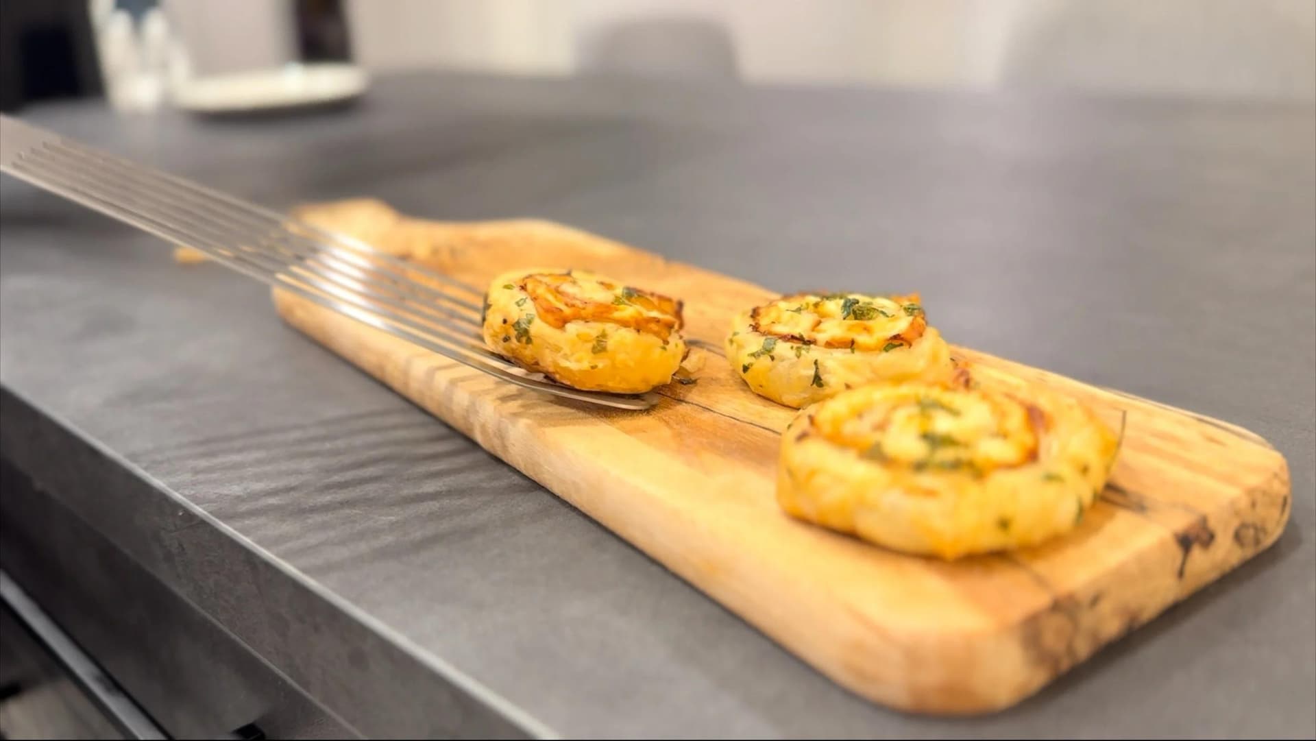 Golden baked ham and cheese pinwheels on a wooden serving board with a pastry brush.
