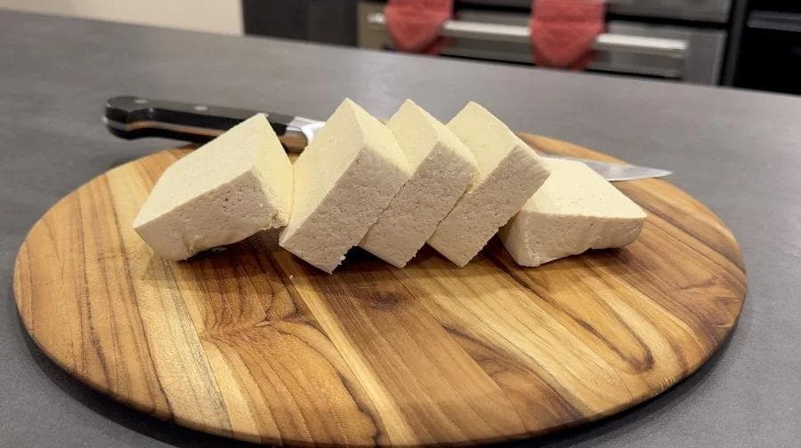 Sliced tofu blocks arranged on a wooden cutting board in a kitchen setting.