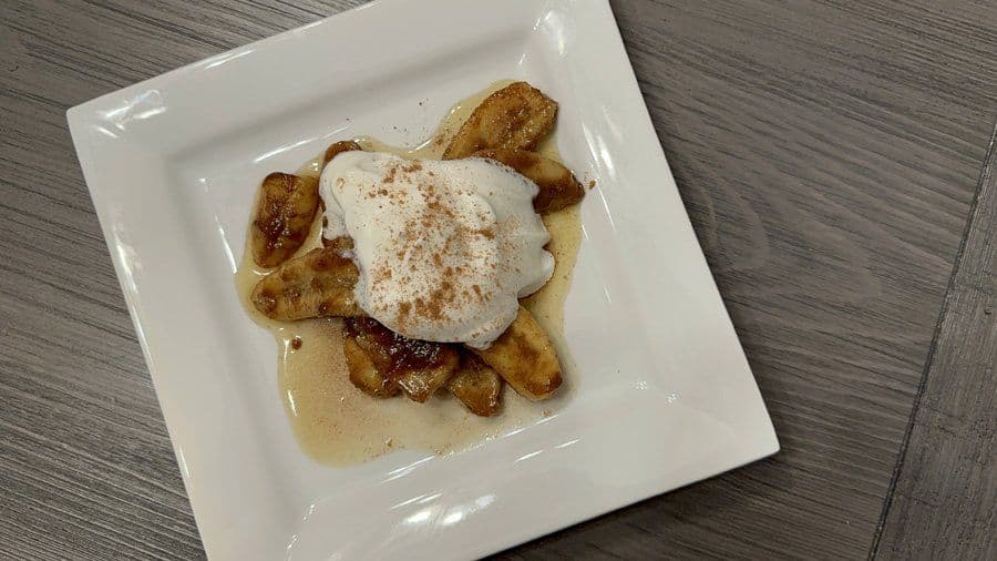 Caramelized banana slices topped with whipped cream and cinnamon on a white plate with caramel sauce.