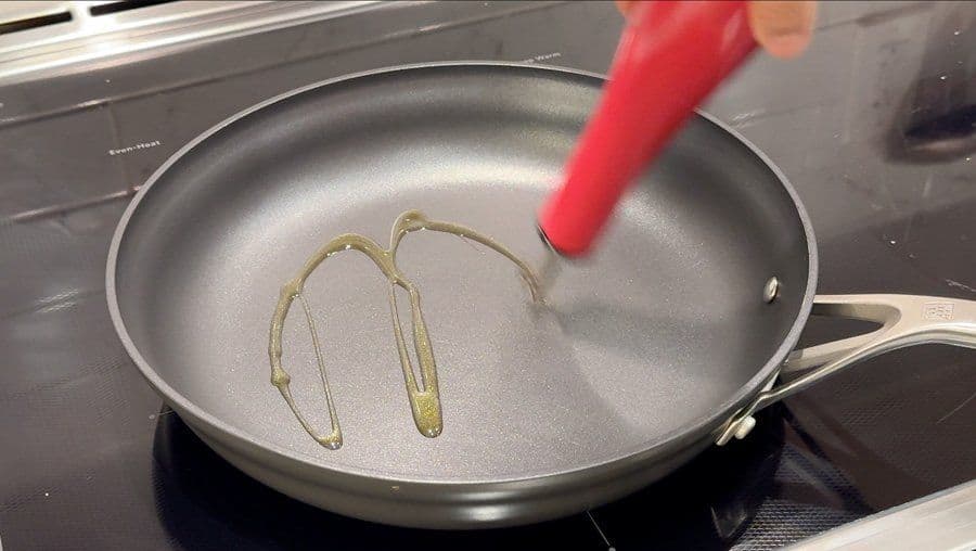 Sautéing sliced shallots in olive oil in a skillet with a red spatula.