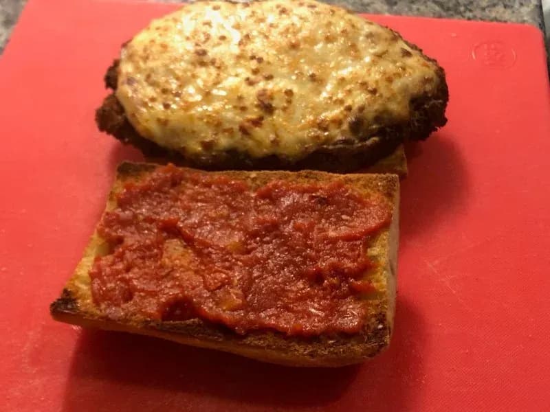 Crispy chicken parmesan sandwich on ciabatta with marinara sauce, sliced in half and served on a red surface.