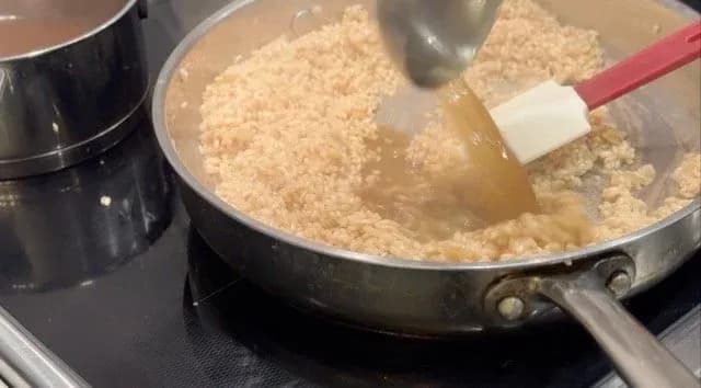 Creamy risotto being stirred in a skillet with a red spatula during the cooking process