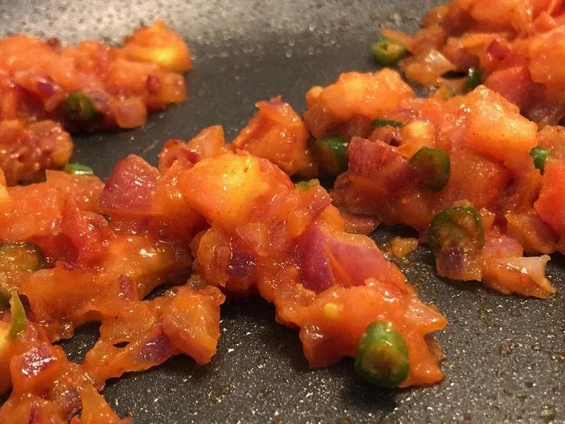 Cooked tomato and green chili masala mixture with melted cheese in a dark pan, ready to be spread on toast.