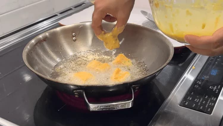 Paneer pakora being fried in hot oil in a wok, with golden pieces floating and bubbling in the oil.
