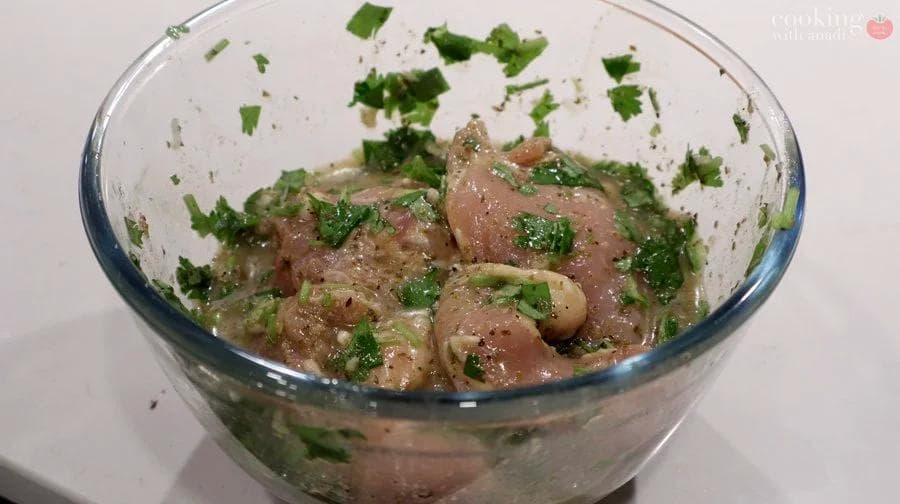 Chicken thighs marinating in mojo sauce with garlic, citrus, cilantro, and olive oil in a glass bowl.