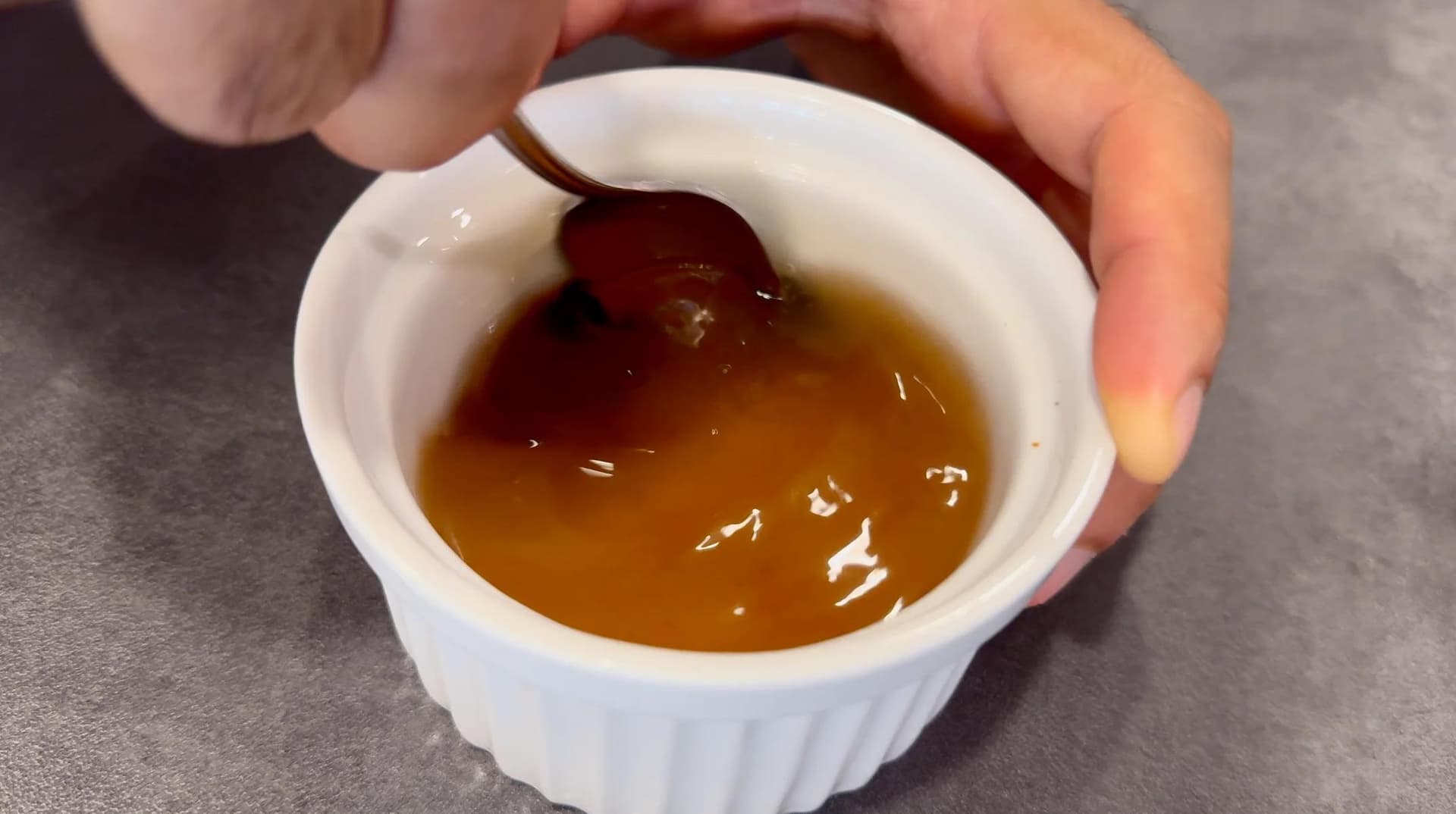 Homemade poutine gravy simmering in a white bowl, showing rich brown color with darker spots of reduced sauce.