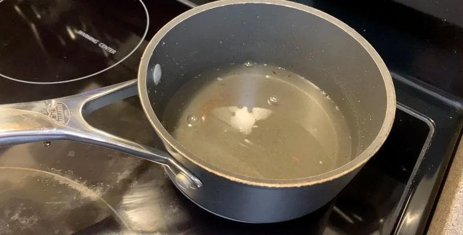 Sugar and water mixture simmering in a saucepan on the stovetop for caramel sauce.