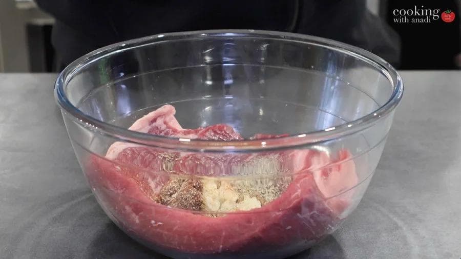Raw flank steak with marinade ingredients in a glass bowl before cooking.
