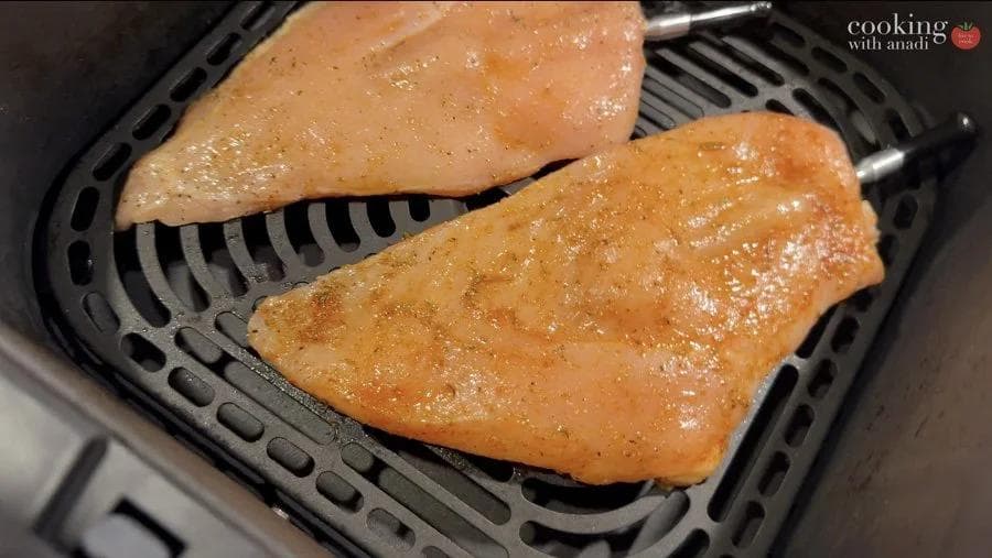 Two seasoned chicken breasts cooking in an air fryer basket, golden brown and glistening.