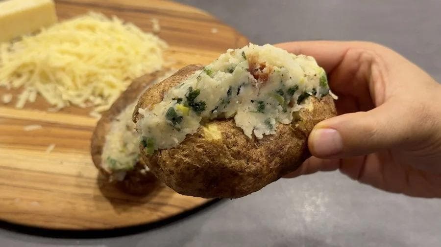 Hand holding an air fryer twice baked potato filled with colcannon, showing the creamy potato and herb filling.
