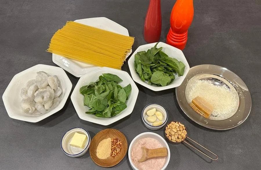 Ingredients laid out for spinach pesto pasta with shrimp: pasta, fresh spinach, shrimp, garlic, butter, cheese, pine nuts, and seasonings.