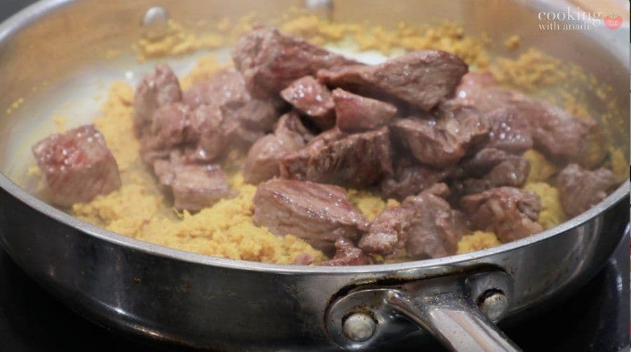 Browned beef chunks cooking in a pan with yellow curry paste and spices.
