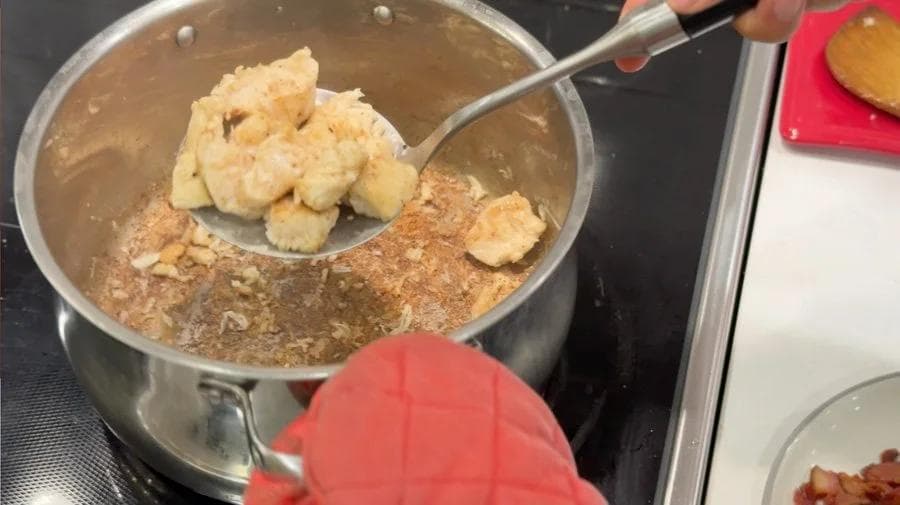 Slotted spoon lifting browned chicken pieces from pot of bacon fat and flour mixture during stew preparation.