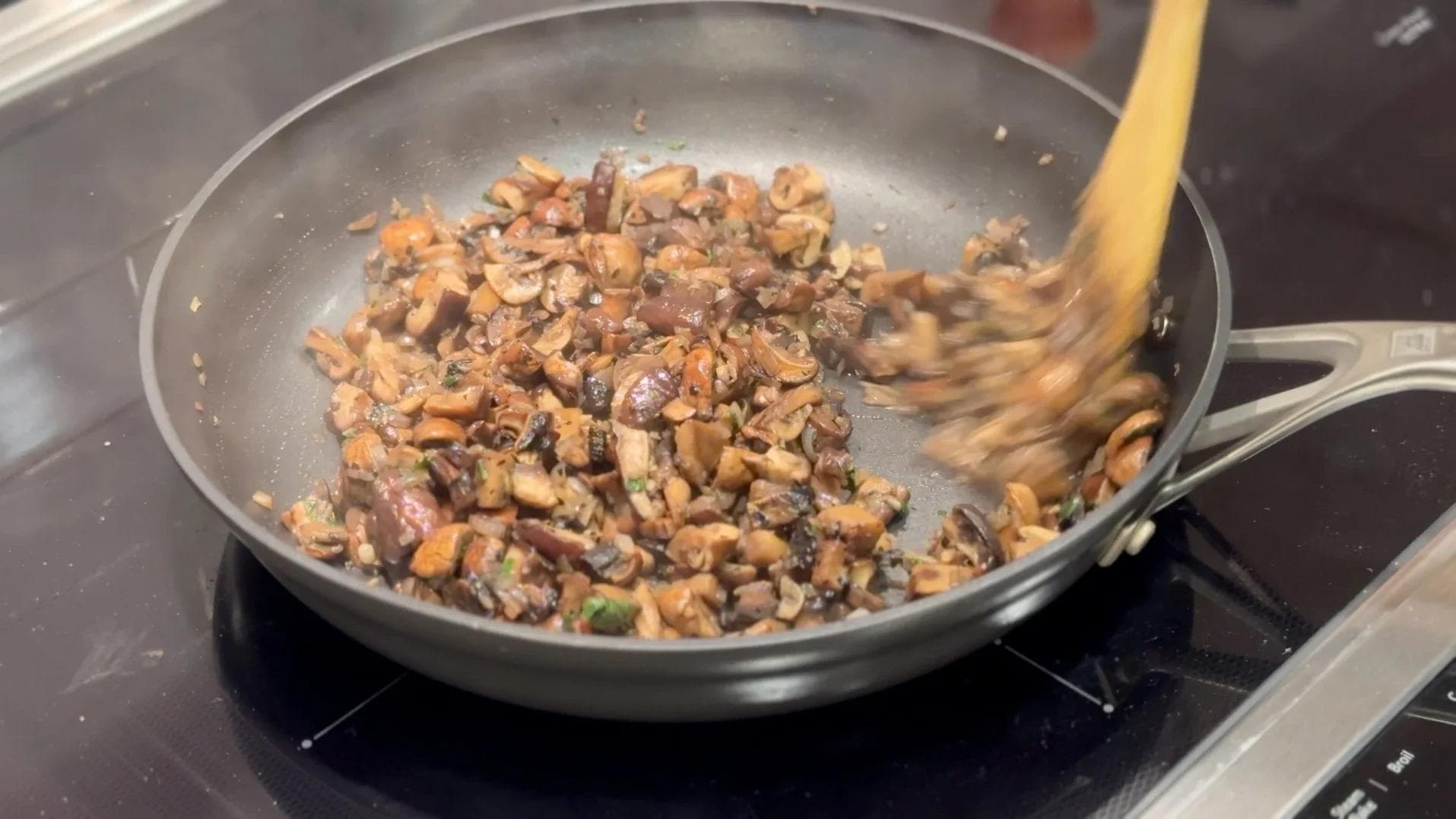 Sautéed mixed mushrooms cooking in a pan with a wooden spatula, showing reduced mushrooms with visible browning.