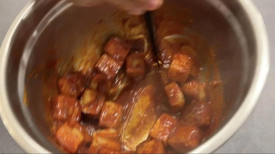 Crispy golden tofu cubes being tossed in brown Korean-style sauce in a white bowl with a spoon.