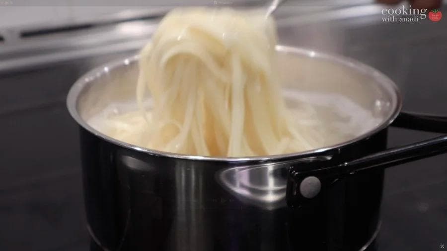 Cooked noodles being lifted from boiling water with chopsticks in a black pot.