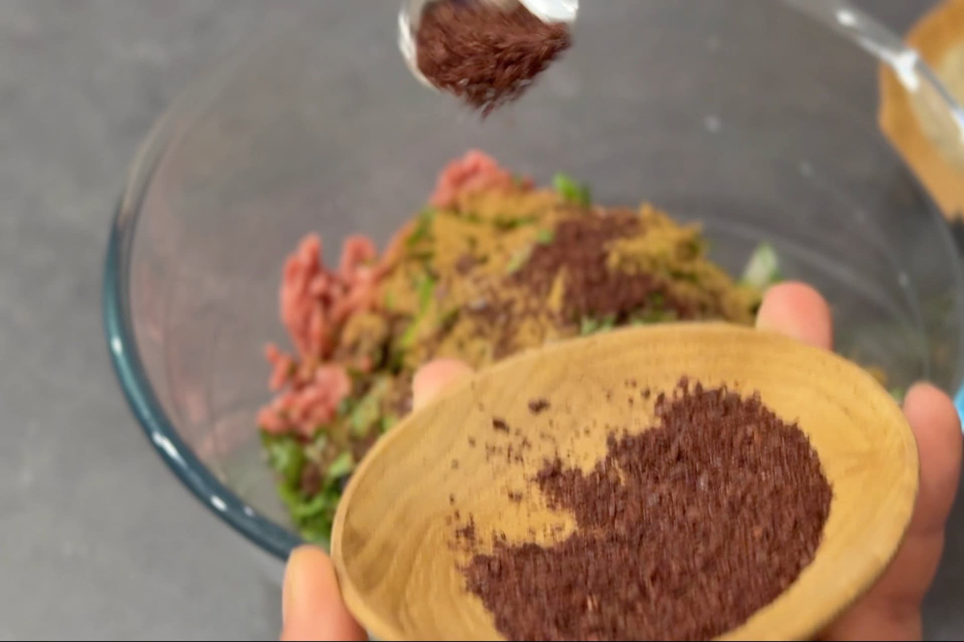 Lebanese seven spice mix being sprinkled onto ground beef mixture in a bowl for kafta preparation.