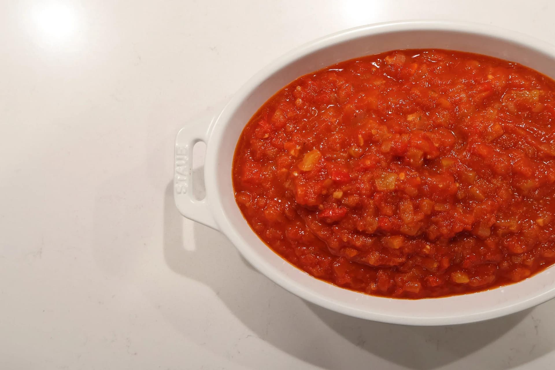 White Staub baking dish filled with chunky Basque piperade, a rich red tomato and pepper sauce