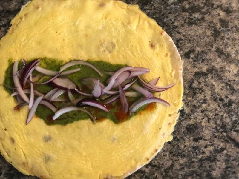 Turmeric-yellow paratha topped with green chutney and sliced red onions arranged in the center.