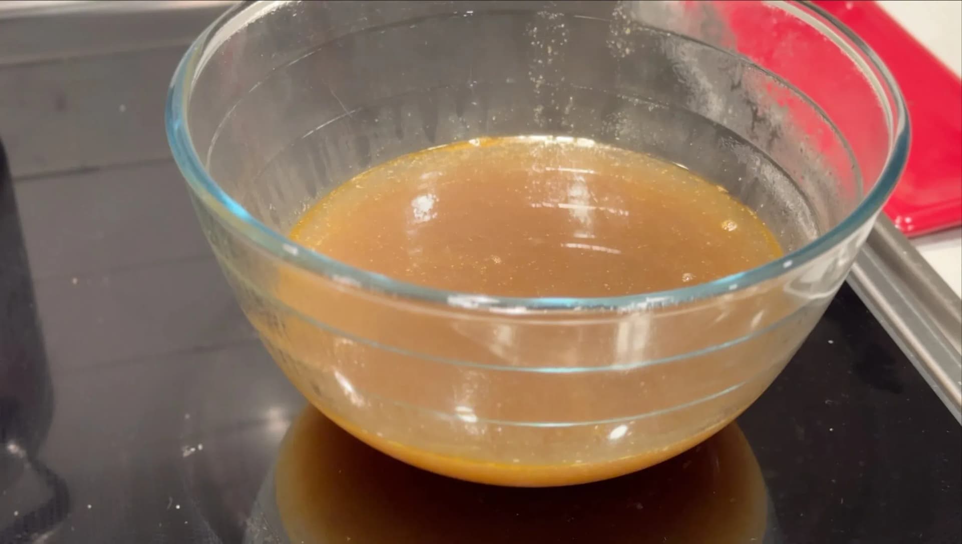 Strained lobster broth in a glass bowl, golden-amber in color, ready for risotto preparation.
