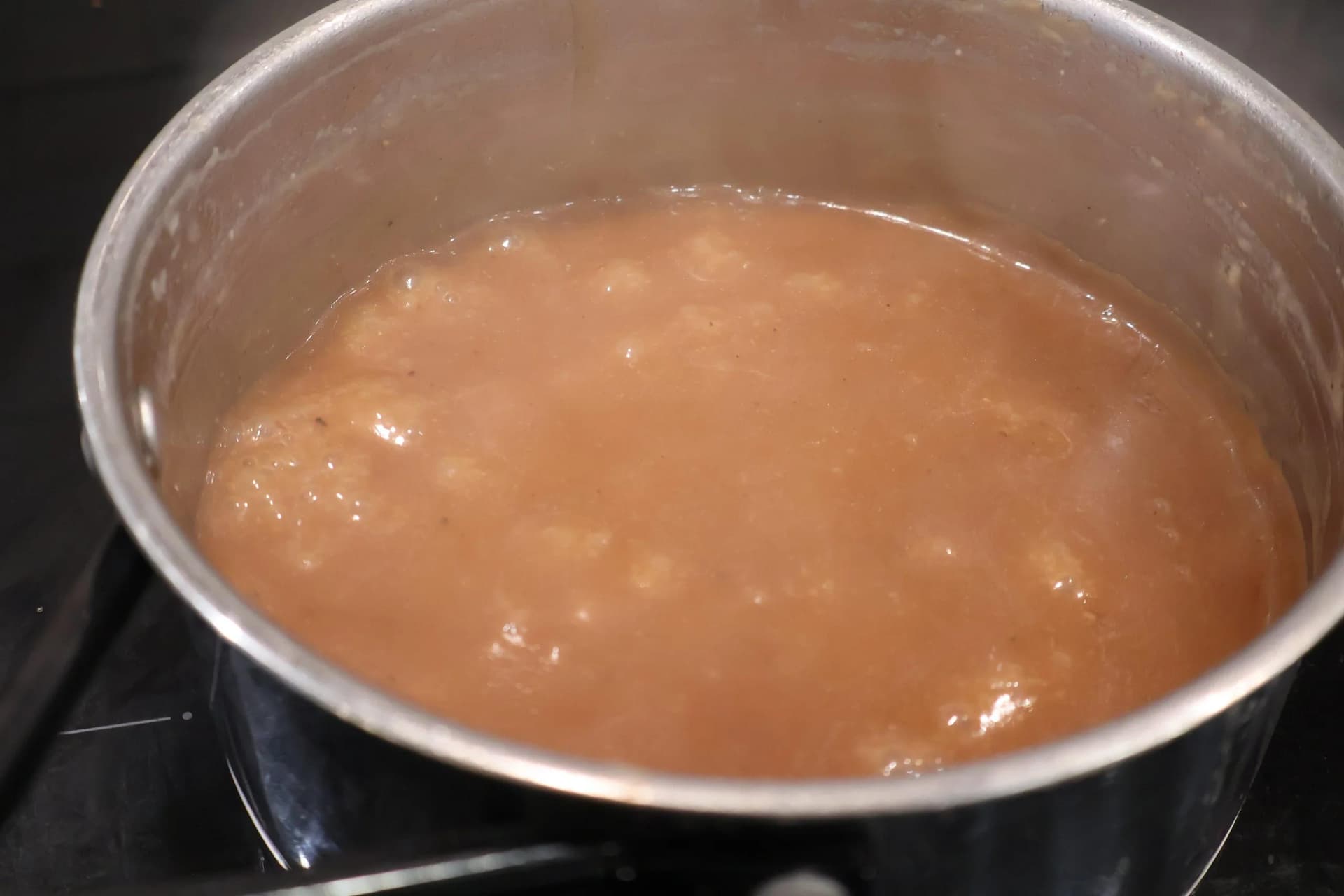 Simmering brown gravy in a pot, reduced and thickened for poutine.