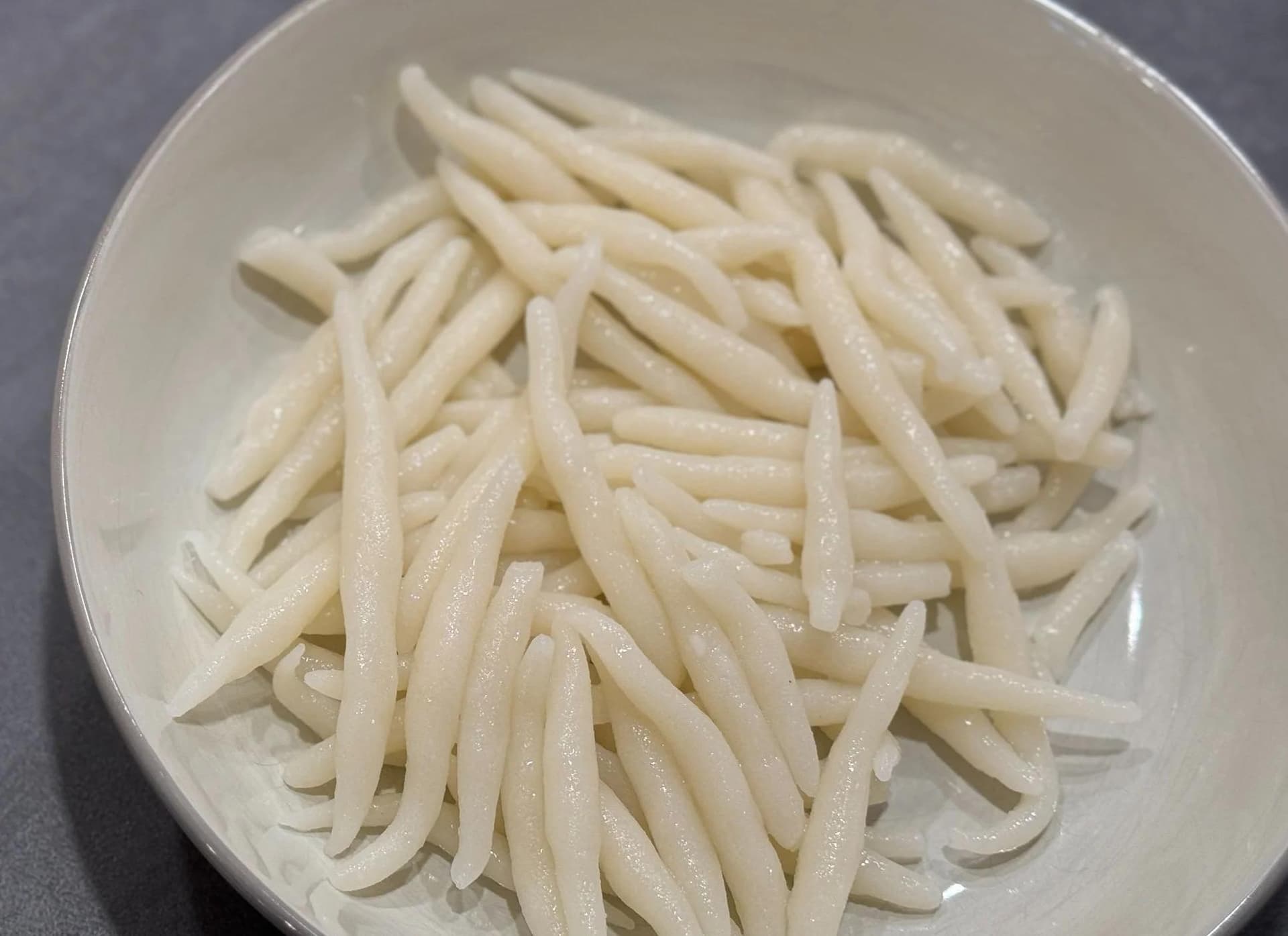 Cooked rice pin noodles piled in a white bowl, thin and translucent with a glossy appearance.